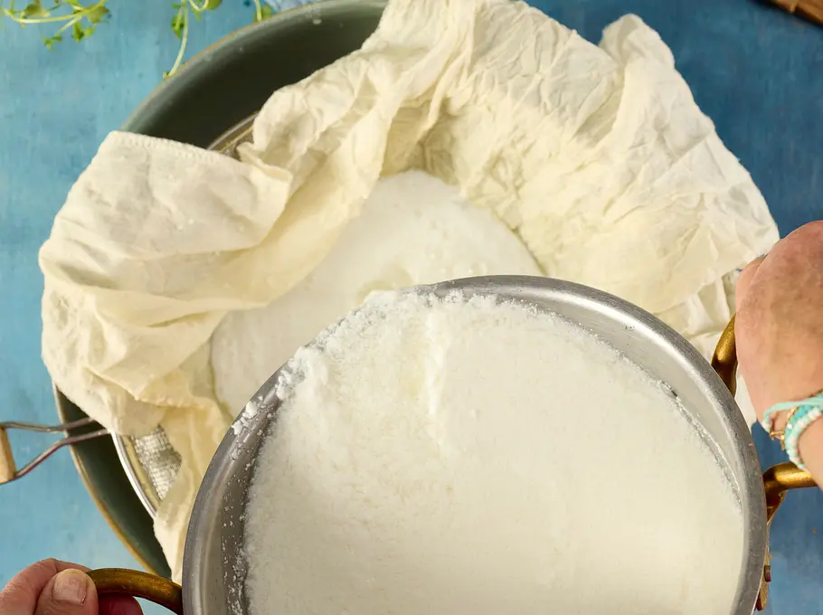 Schneller „Ricotta“ alla casa Rezept Die geronnene Milchmischung wird aus dem Topf in ein mit Mulltuch ausgelegtes Sieb gegossen, um die Molke abzutrennen.