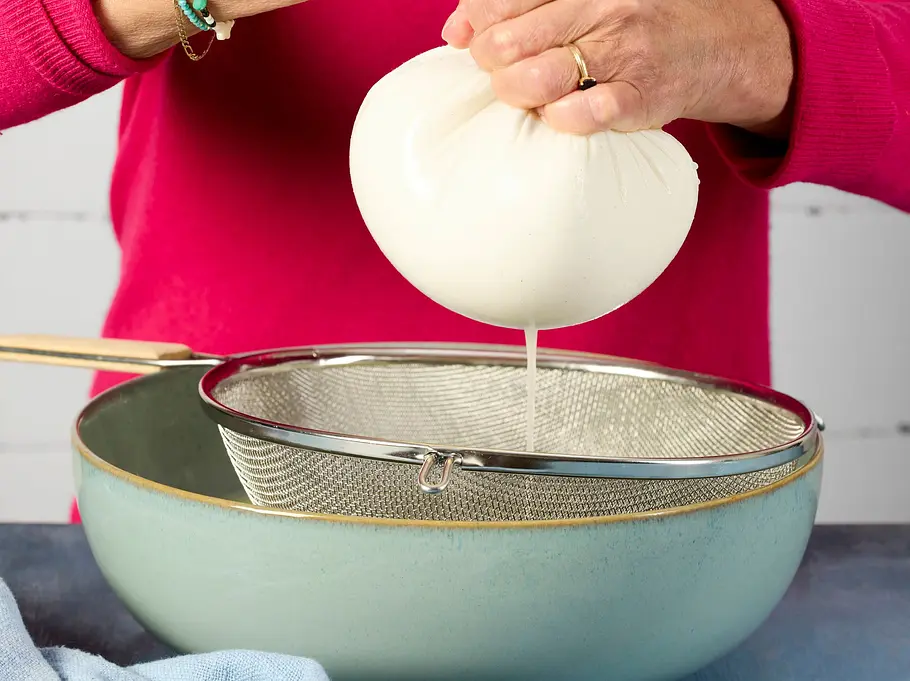 Schneller „Ricotta“ alla casa Rezept Die Ricottamasse wird in einem Mulltuch kräftig ausgepresst, sodass überschüssige Molke durch das Tuch in eine Schüssel tropft.