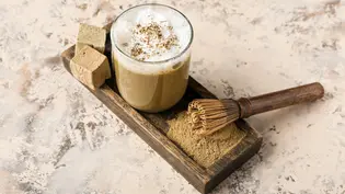 Auf einer hölzernen Palette steht ein Glas mit Hojicha-Latte neben einem Bambusbesen und dem gemahlenen Hojicha-Grüntee-Pulver - Foto: LECKER @ Bauer Media Group / Pixelshot Auf einer hölzernen Palette steht ein Glas mit Hojicha-Latte neben einem Bambusbesen und dem gemahlenen Hojicha-Grüntee-Pulver - Foto: LECKER @ Bauer Media Group / Pixelshot