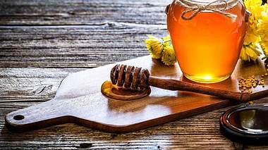 Honiglöffel und Honig im Glas auf einem Holzbrett - Foto: iStock