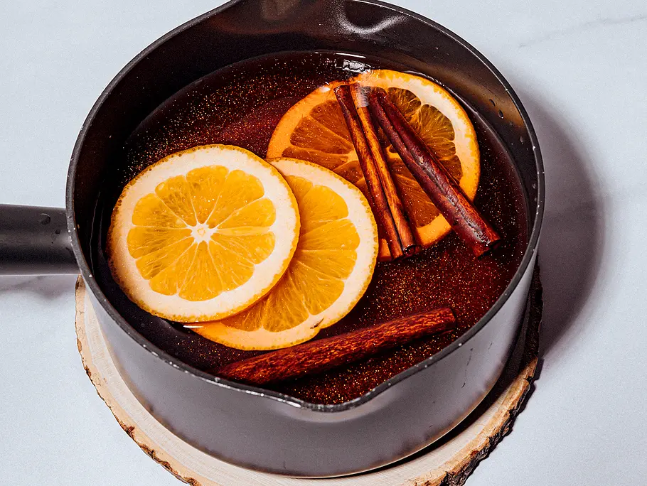 Ein schwarzer Topf, gefüllt mit Hot Glitter Spritz, in der glitzernen Fküssigkeit liegen 3 Orangenscheiben und 3 Zimtstangen