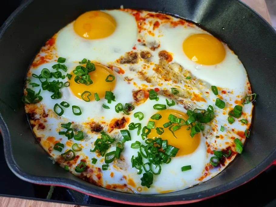 Hot Honey Eggs in Pfanne Spiegeleier in Pfanne mit Lauchzwiebelringen.