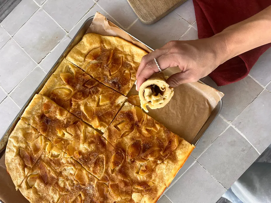 Apfelpfannkuchen vom Blech Apfelpfannkuchen vom Blech mit einer Hand, die ein Stück eingerollt hält.