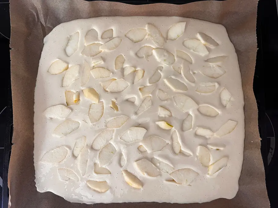 Pfannkuchenteig mit Apfelstücken Apfelpfannkuchenteig wird auf dem Blech mit Apfelscheiben belegt.