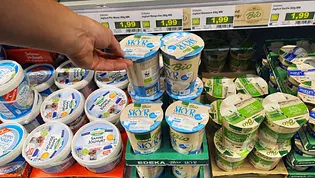 Hand greift im Supermarktregal nach einem Becher Skyr zwischen anderen Joghurtprodukten; Preisschilder und verschiedene Sorten sind sichtbar. - Foto: @Imago-Images