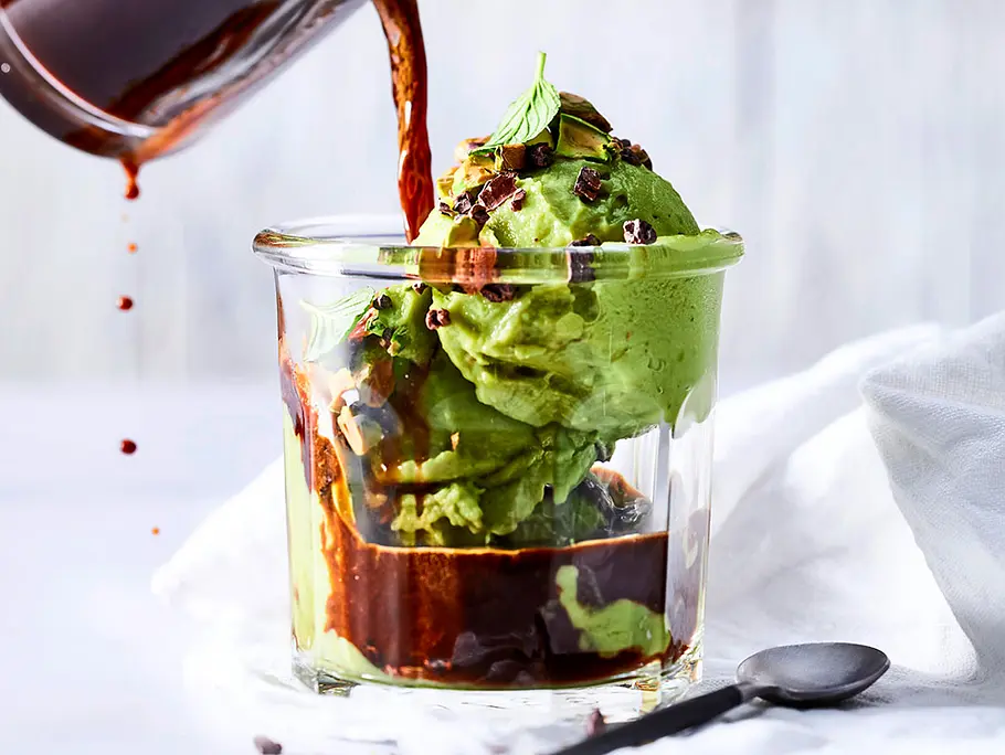 Ein Glas mit zwei Kugeln selbst gemachter Pistazien-Nicecream, auf die gerade aus einer Glaskanne frischer Espresso gekippt wird.