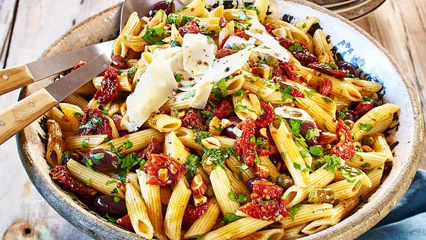 Italienischer Nudelsalat mit getrockneten Tomaten und Parmesansplitter in einer großen rustikalen Schüssel mit Servierbesteck - Foto: House of Food / Bauer Food Experts KG