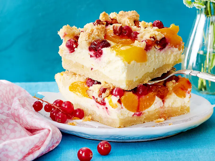 Johannisbeer-Aprikosen Kuchen Rezept Zwei viereckige Johannisbeer-Aprikosen-Kuchen-Stücke auf einem kleinen Teller serviert. Ein Stück wird auf einer Gabel gerade serviert. Der Teller ist mit einem kleinen Strauch Johannisbeeren verziert. Rezept