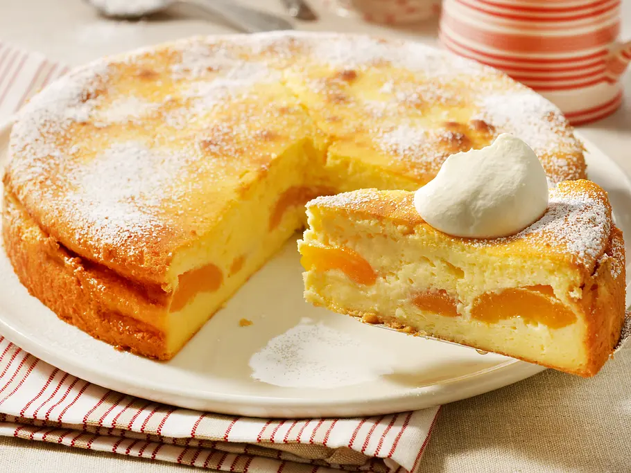 Ein angeschnittener Käsekuchen ohne Boden, bei dem durch den Anschnitt die Aprikosen im Inneren sichtbar werden