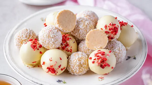 Mehrere Käsekuchen-Pralinen mit weißer Schokolade und Kokosraspel auf einem Teller - Foto: ShowHeroes für LECKER @ Bauer Media Group