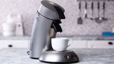Seitenansicht von einer silbernen Senseo-Kaffeepadmaschine mit einer weißen Kaffeetasse auf der Ausgabefläche in einer hellen Küche. - Foto: LECKER @ Bauer Media Group / Istock / AndreyPopov Seitenansicht von einer silbernen Senseo-Kaffeepadmaschine mit einer weißen Kaffeetasse auf der Ausgabefläche in einer hellen Küche. - Foto: LECKER @ Bauer Media Group / Istock / AndreyPopov