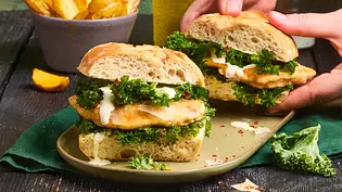 Krosses Ciabatta-Sandwich gefüllt mit gebratenem Hähnchenfilet, frischem Grünkohl und cremiger Sauce, serviert auf einem grünen Teller mit goldenen Pommes in einer Schale im Hintergrund. - Foto: LECKER @ Bauer Media Group