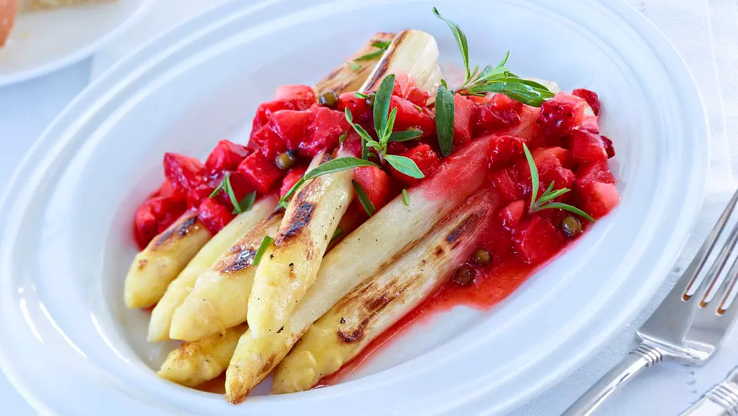 Ein ovaler Teller mit weißen Spargelstangen und Erdbeersoße mit Erdbeerstücken und Kräutern. - Foto: LECKER @ Bauer Media Group