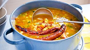 Ein großer Emailletopf voll mit stückiger Kartoffel-Kürbissuppe und 2 gebratenen Merguez-Würstchen, im Topf eine Suppenkelle. - Foto: LECKER @ Bauer Media Group