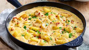 Kartoffelstückchen in cremiger Sauce mit Speckwürfeln und frischer Petersilie in einer schwarzen Pfanne auf Holztisch. - Foto: LECKER @ Bauer Media Group