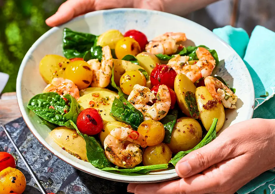 Kartoffelsalat mit Garnelen und Grilltomaten Kartoffelsalat mit Garnelen und Grilltomaten in einem großen Teller der von 2 Händen gehalten wird