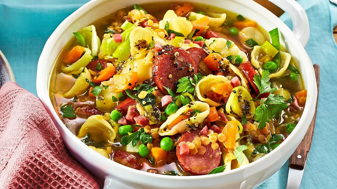 Eine große weiße Schüssel mit einem bunten Eintopf aus Linsen, Erbsen, Wurstscheiben und Muschelnudeln. - Foto: LECKER @ Bauer Media Group