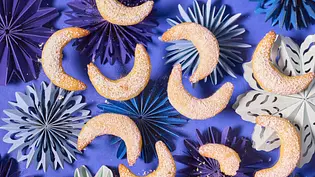 Halbmondförmige Kipferl „Golden Milk“, bestäubt mit gelbem Puder, auf blauen und lilafarbenen Papierstern-Unterlagen auf lilafarbener Oberfläche angerichtet. - Foto: LECKER @ Bauer Media Group