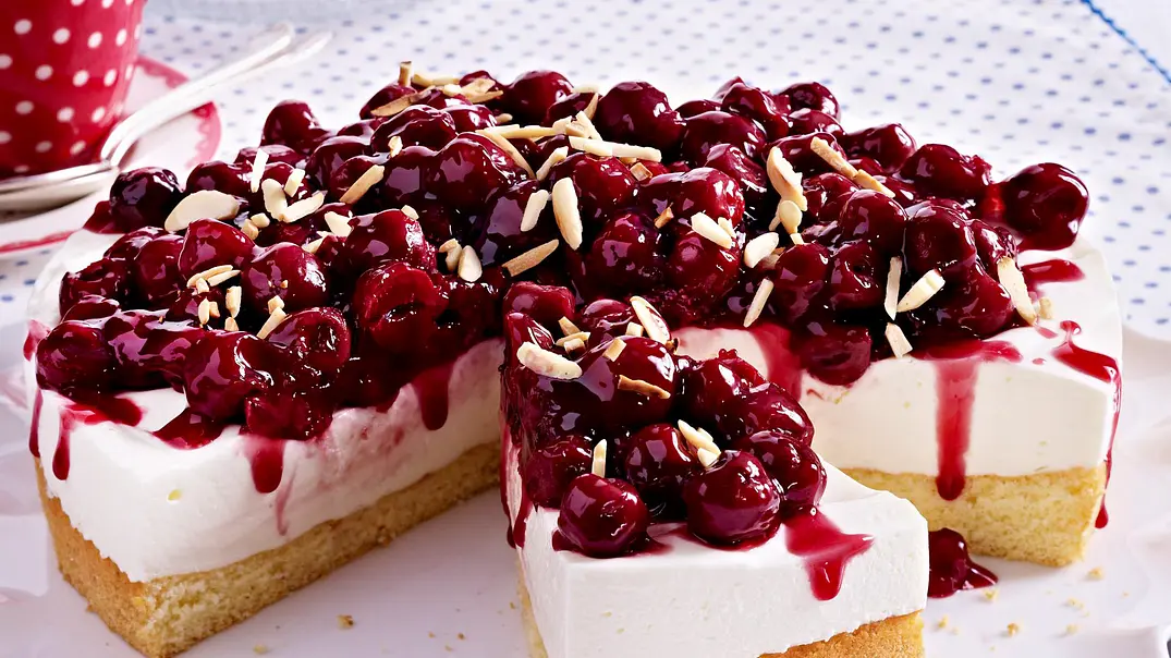 Runder Kirsch-Quark-Kuchen mit Mandelstiften bestreut und auf einem gewelltem weißem Teller serviert.  - Foto: LECKER @ Bauer Media Group