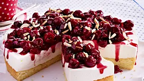 Runder Kirsch-Quark-Kuchen mit Mandelstiften bestreut und auf einem gewelltem weißem Teller serviert.  - Foto: LECKER @ Bauer Media Group