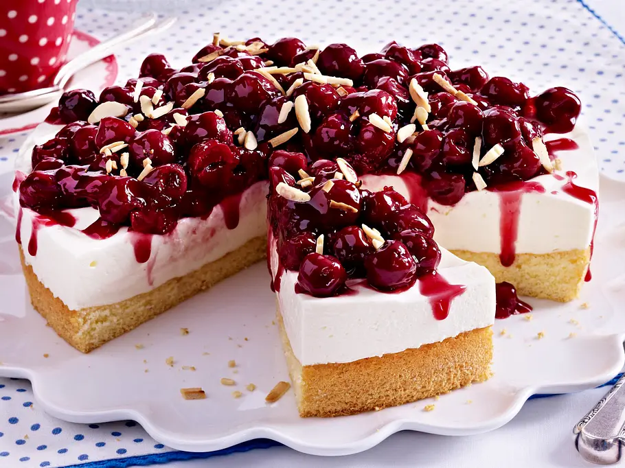 Kirsch-Quark-Torte Rezept Runder Kirsch-Quark-Kuchen mit Mandelstiften bestreut und auf einem gewelltem weißem Teller serviert.