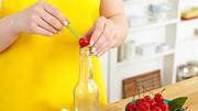 Eine Kirsche liegt zum Entkernen auf der Öffnung einer Glasflasche. Mit einem grünen Essstäbchen wird oben in die Kirsche gestochen, um den Kern unten herauszudrücken. - Foto: House of Food / Bauer Food Experts KG