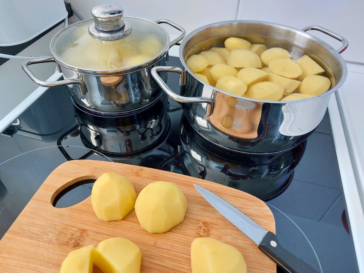 Kartoffeln kochen in zwei Töpfen auf dem Herd, auf einem Brett werden Kartoffeln geschnitten