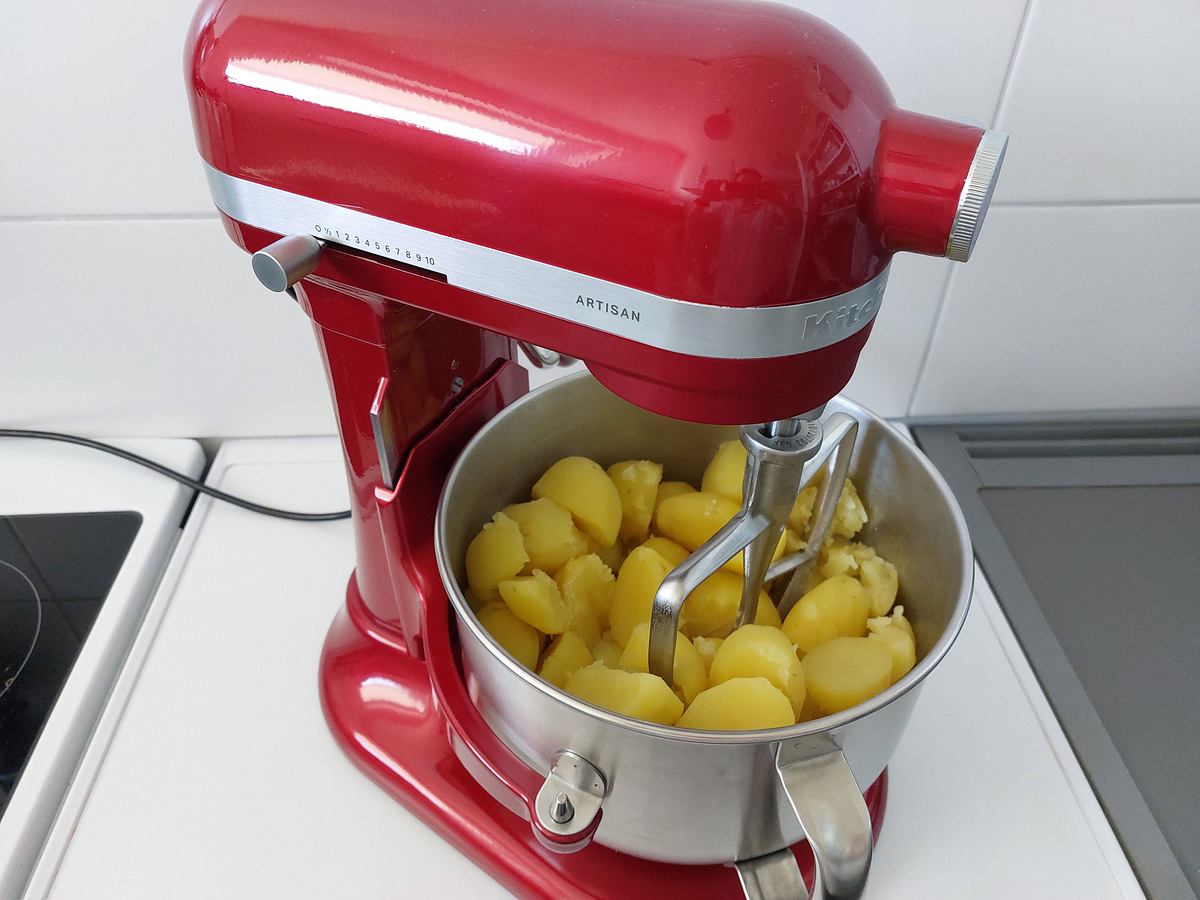 Gekochte Kartoffeln liegen in einer Metallschüssel einer roten KitchenAid Küchenmaschine, bereit zum Pürieren.