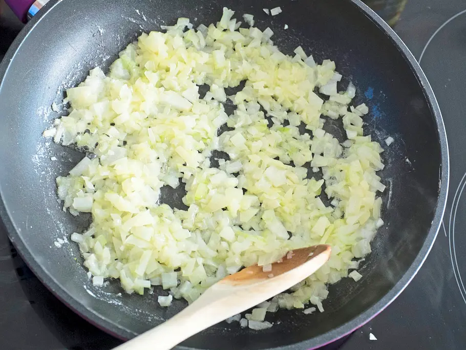 Fein gewürfelte Zwiebeln werden in einer Pfanne auf dem Herd in Butter glasig gedünstet und mit einem Holzlöffel umgerührt.