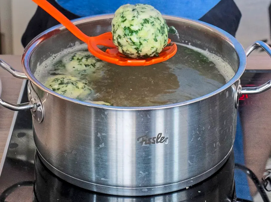 Spinat-Ricotta-Klöße werden mit einer Schaumkelle in einen großen Topf mit siedendem Salzwasser gegeben.