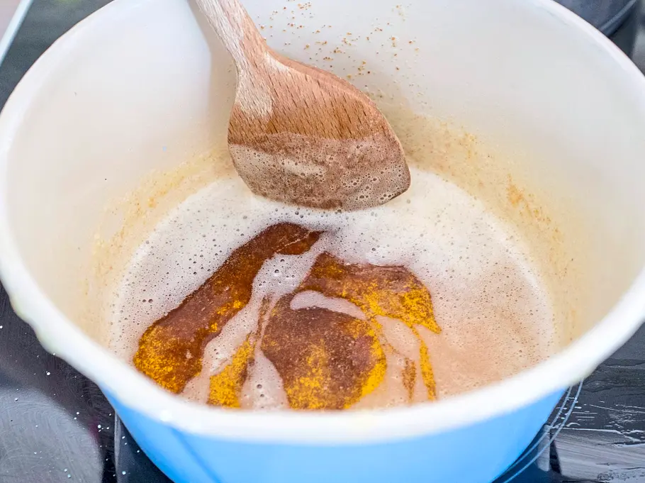 In einem hellblauen Topf wird Butter mit Semmelbröseln aufgeschäumt und goldbraun gebräunt, ein Holzlöffel rührt darin.