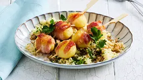 Knödel-Speck-Spieße auf einem Bett aus lockerem Couscous mit frischer Petersilie, angerichtet auf einem geriffelten Teller mit hellblauer Serviette. - Foto: LECKER @ Bauer Media Group Knödel-Speck-Spieße auf einem Bett aus lockerem Couscous mit frischer Petersilie, angerichtet auf einem geriffelten Teller mit hellblauer Serviette. - Foto: LECKER @ Bauer Media Group