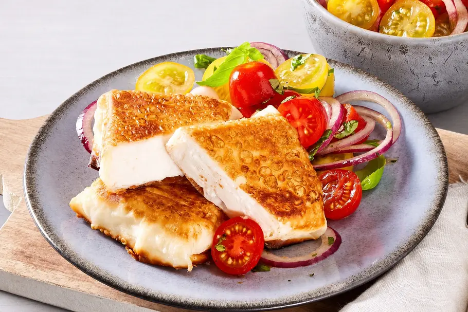 Knuspriger Feta aus dem Airfryer mit Tomatensalat Knuspriger Feta aus dem Airfryer mit Tomatensalat mit Tomatensalat aus gelben und roten Kirschtomaten und roten Zwiebeln auf einem grauen Teller.