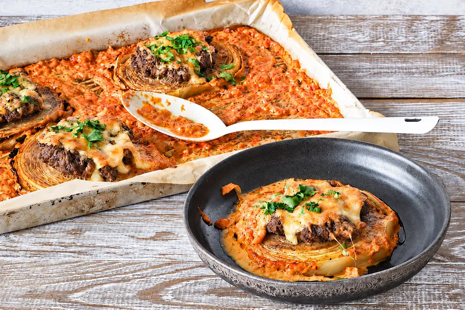 Geniale Kohl-Steaks aus dem Ofen: mit Hack, Käse und cremiger Sauce überbacken Käseüberbackenes Hackfleisch auf Kohlscheiben liegt in orangefarbener Sauce auf einem Backblech und einem dunklen Teller.