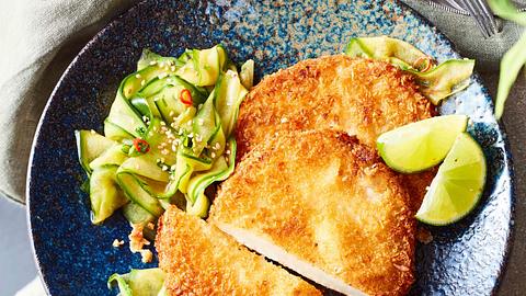 Goldbaune Kohlrabischnitzel zu Asia-Gurkensalat auf einem dunkelblauen Teller mit Limettenspalten - Foto: House of Food / Bauer Food Experts KG