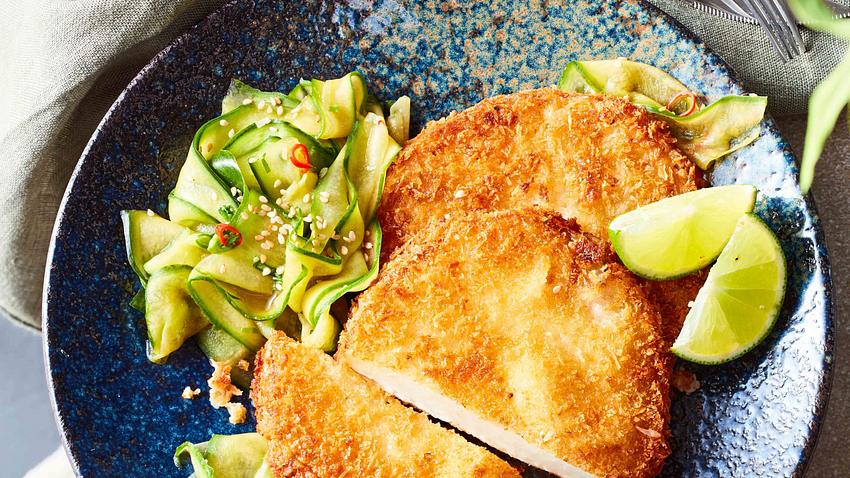 Goldbaune Kohlrabischnitzel zu Asia-Gurkensalat auf einem dunkelblauen Teller mit Limettenspalten - Foto: House of Food / Bauer Food Experts KG