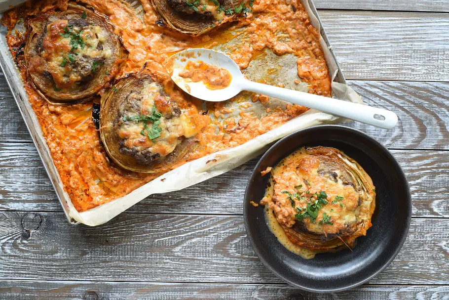 Überbackene Kohlstücke mit Kräutern liegen in orangefarbener Sauce auf einem Backblech und einem schwarzen Teller.