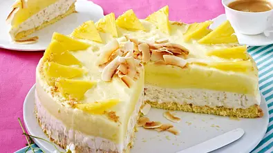 Kokos-Ananas-Eistorte auf einem weißen Teller steht auf einem gedeckten Kaffeetisch. - Foto: LECKER @ Bauer Media Group