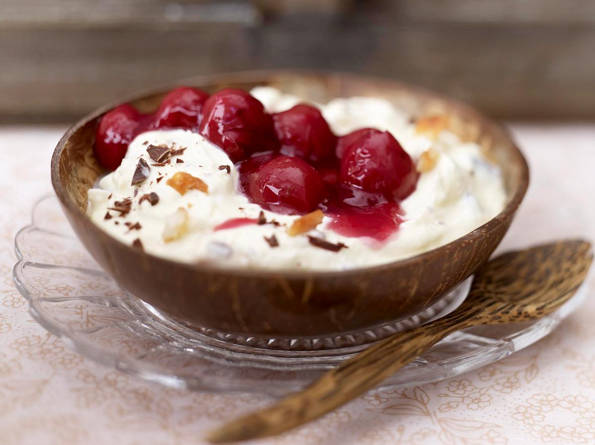 Kokosmakronen-Creme mit Kirschen Kokos-Mascarpone-Creme mit Kirschtopping in einer braunen Dessertschale