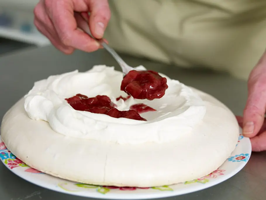 Rhabarberkompott wird mit einem Löffel auf der Sahne in der Mulde der Pavlova verteilt.