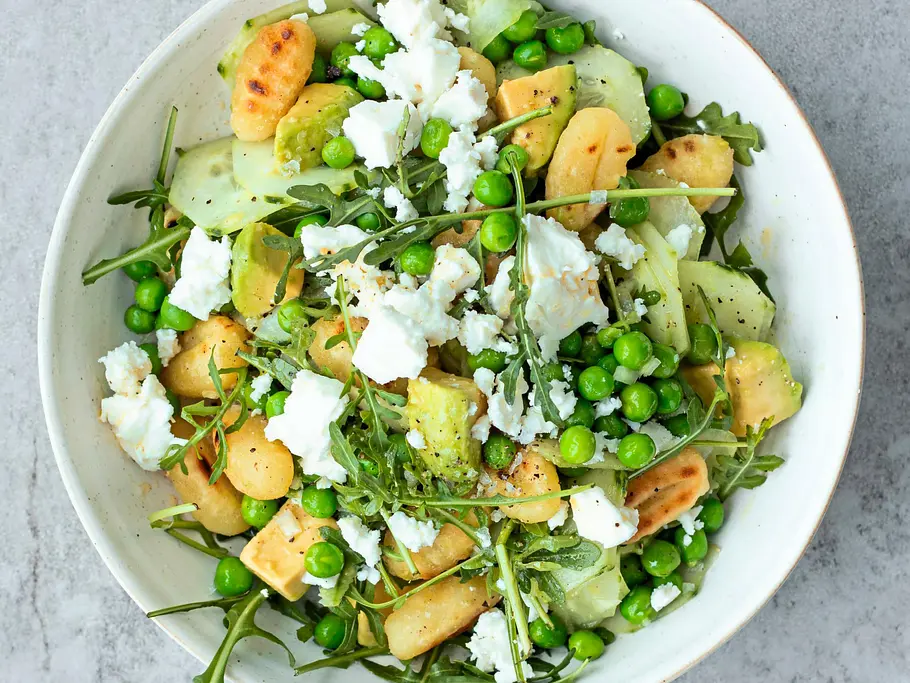 Bunter Gurkensalat mit gebratenen Gnocchi, Erbsen, Rucola und zerbröseltem Feta auf einem weißen Keramikteller.