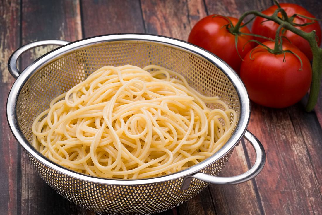 Spaghetti in einem Stahl-Küchensieb auf einer Holzoberfläche