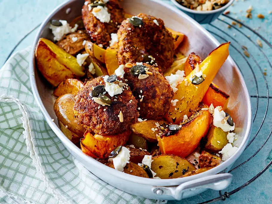 Kürbis-Blätterteig-Taschen Ovale weiße Auflaufform mit Kürbisfrikadellen, Kartoffel- und Kübisspalten und Feta.