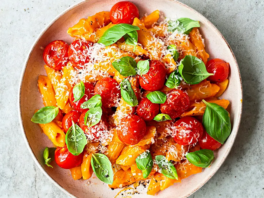 Cremige Kürbis-Pasta mit gerösteten Kirschtomaten, frischem Basilikum und geriebenem Parmesan in einer hellen, runden Schale.