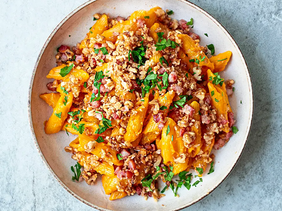 Kürbis-Pasta mit knusprigem Bacon-Walnuss-Crunch und frischer Petersilie in einer hellen, runden Schale.