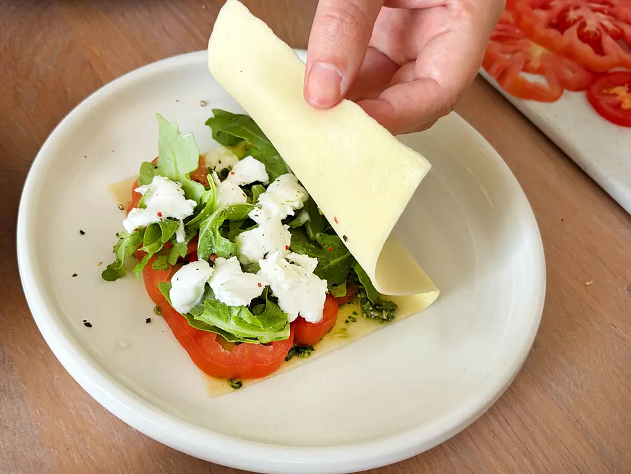 Lasagneblätter falten Eine mit Rucola, Burrata, Tomate und grünem Pesto gefüllte Lasagneplatte wird gefaltet.