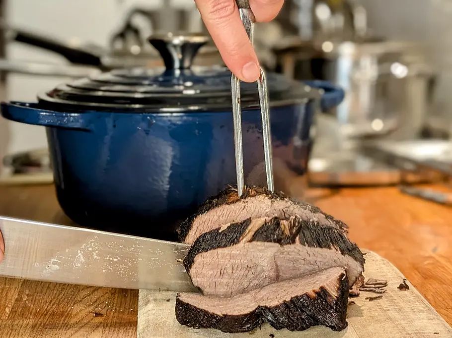Ein fertig gegartes Stück Rindfleisch wird auf einem Holzbrett in Scheiben geschnitten.