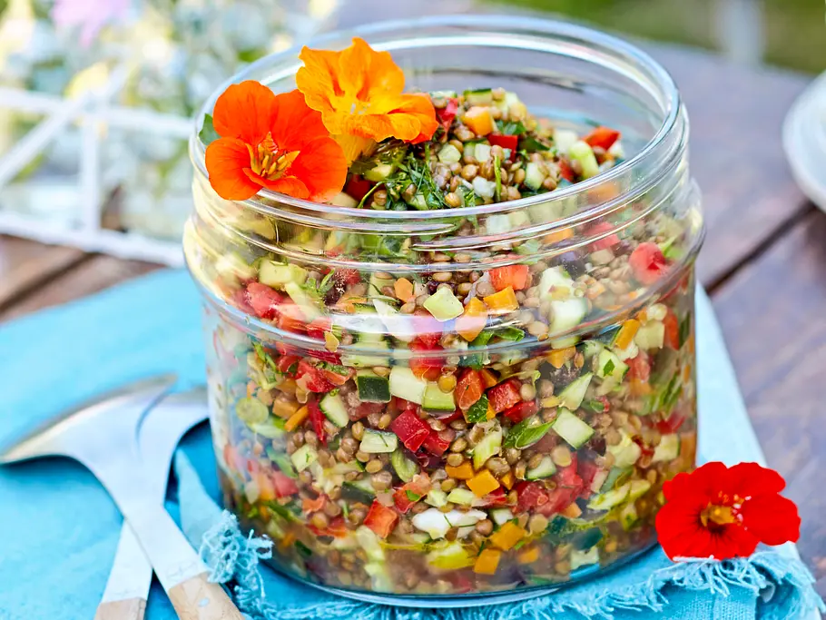 Linsensalat aus dem Glas Ein offenes Einmachglas mit buntem Linsensalat gefüllt und mit Kapuzinerkresse garniert auf einem Holztisch