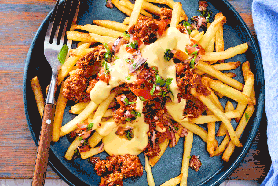 Pommes mit würziger Hackfleischsoße, cremiger Käsesoße und frischer Salsa auf einem dunklen Teller angerichtet.