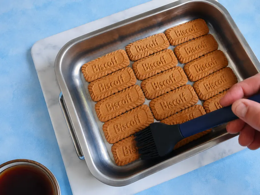Lotus-Tiramisu zubereiten Lotus-Kekse liegen in Auflaufform und werden mit Hilfe eines Silikonpinsels mit Kaffee getränkt.